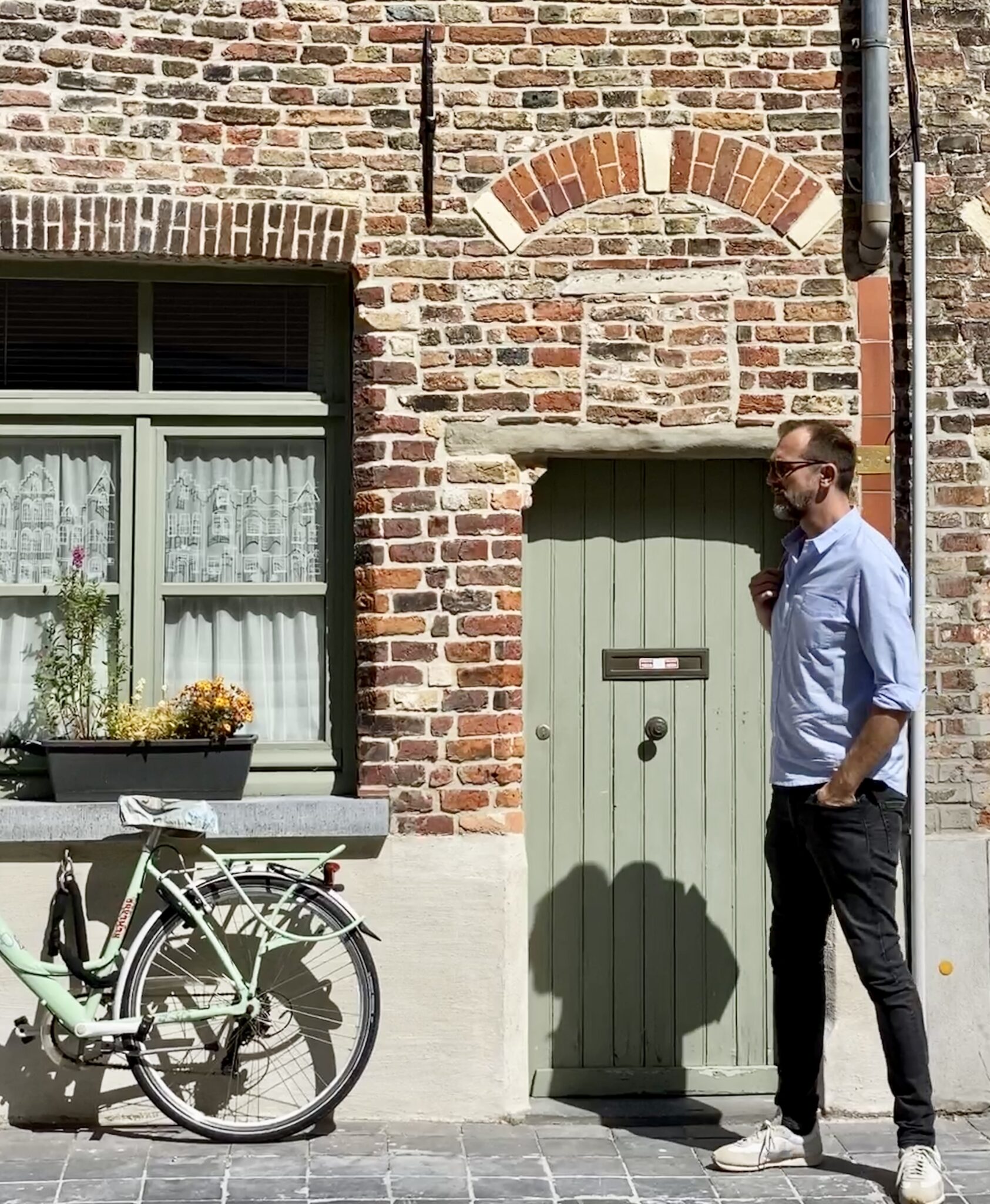 Michael vor hübscher Häuserfront aus roten Backsteinen. Die Farbe der Tür passt zur Farbe des Fahrrads, das an der Hauswand lehnt: mintgrün