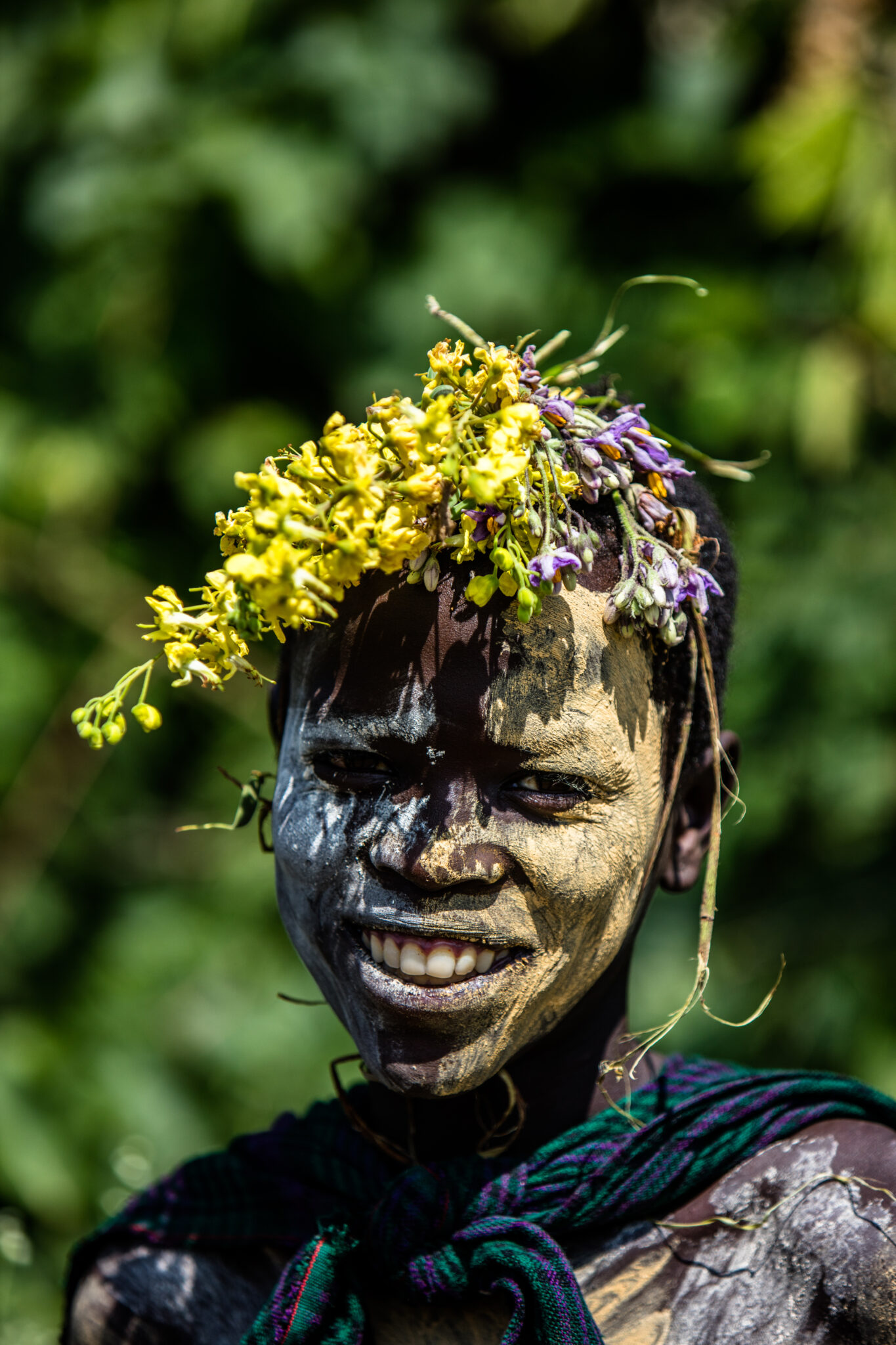 Foto von Farin Urlaub, bemaltes und mit Farbe und Blüten geschmücktes Kind in Äthiopien blickt lächelnd in die Kamera