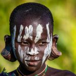 Kind in Äthiopien mit weißer Farbe im Gesicht und großen Ohrpflöcken in den Ohrläppchen