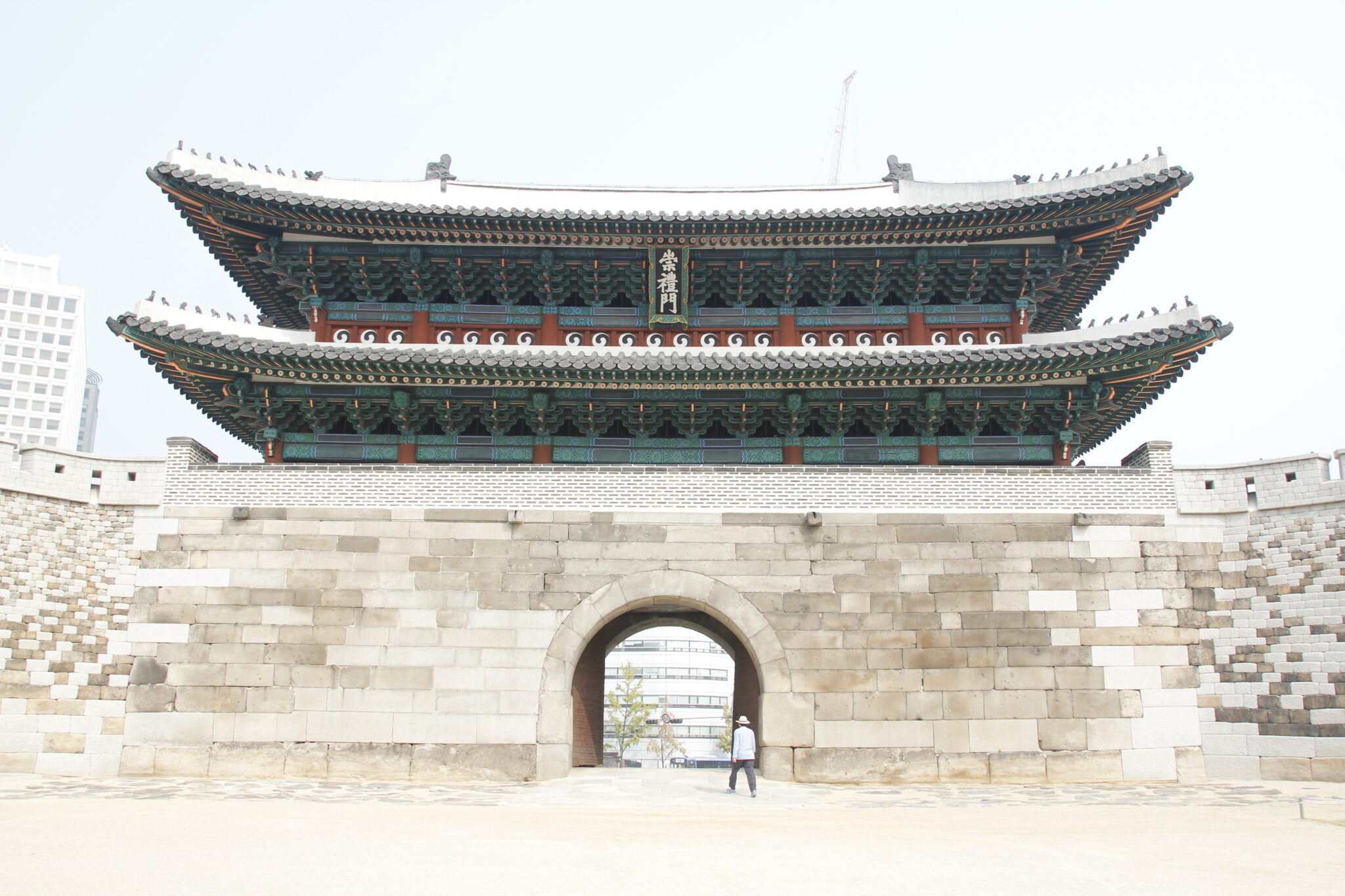 Tempel in Südkorea mit Stadtkulisse dahinter. Ein Mann steht vorm Tor. Helles Licht, heller Sandstein. Reise-Trends 2023