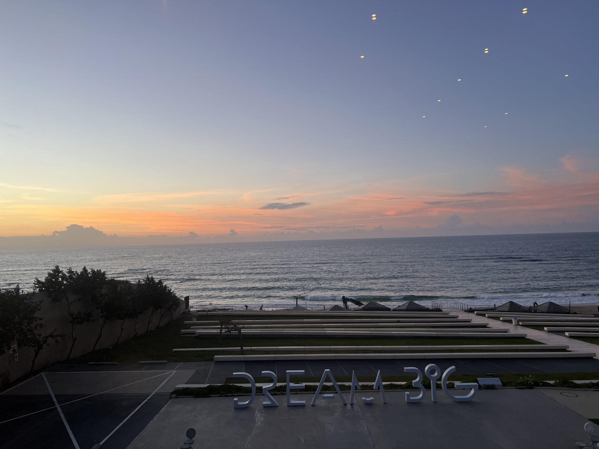 Vor dem Peres Center for Peace and Innovation in Tel Aviv steht eine typografische Skulptur: „Dream Big“. Im Hintergrund sieht man das Meer, darüber ein pastelliger Himmel in der Abenddämmerung