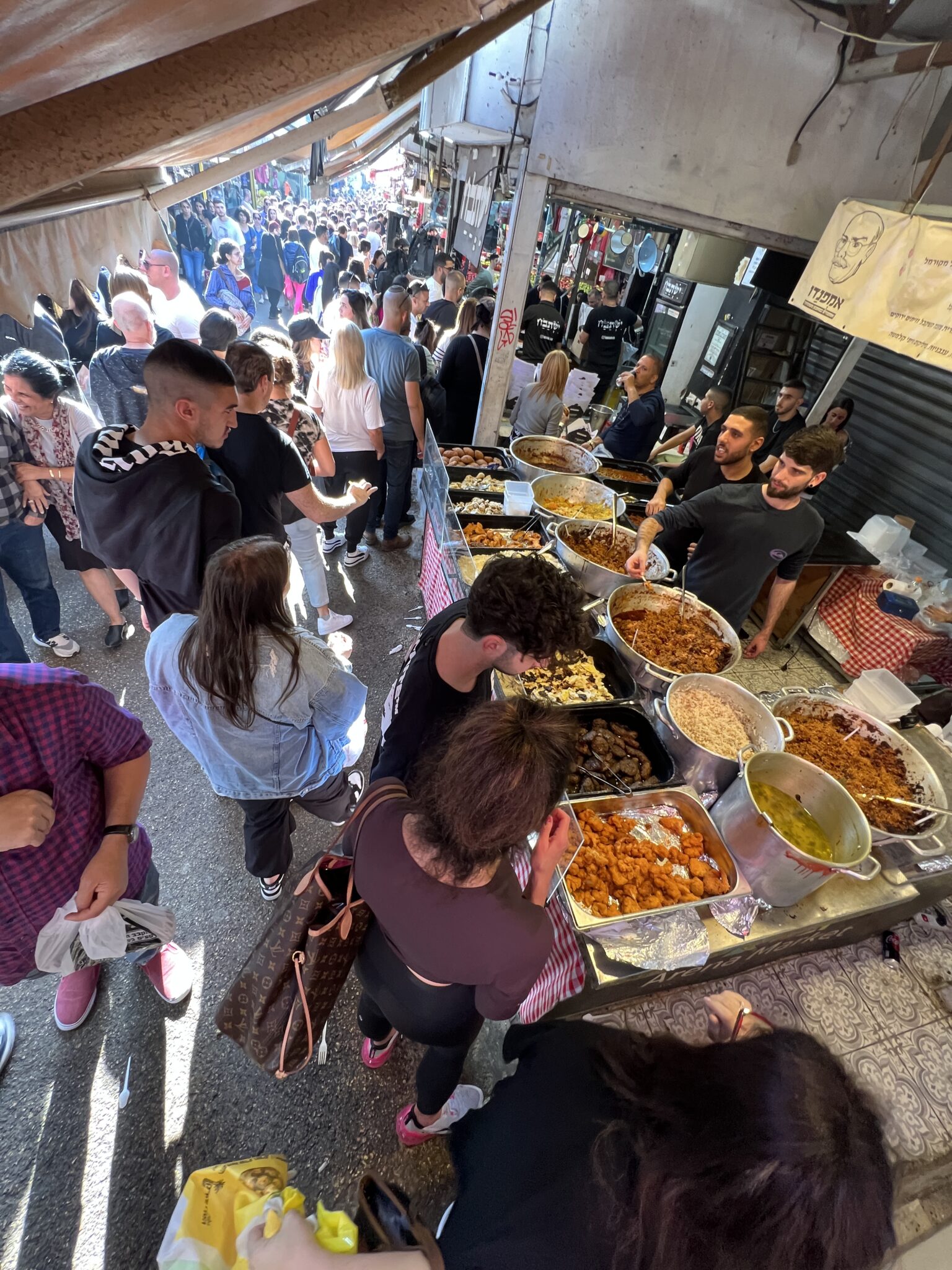 Viele Menschen auf dem Carmel Markt an einem Stand, an dem viele bunte Speisen angeboten werden. Reges Treiben.