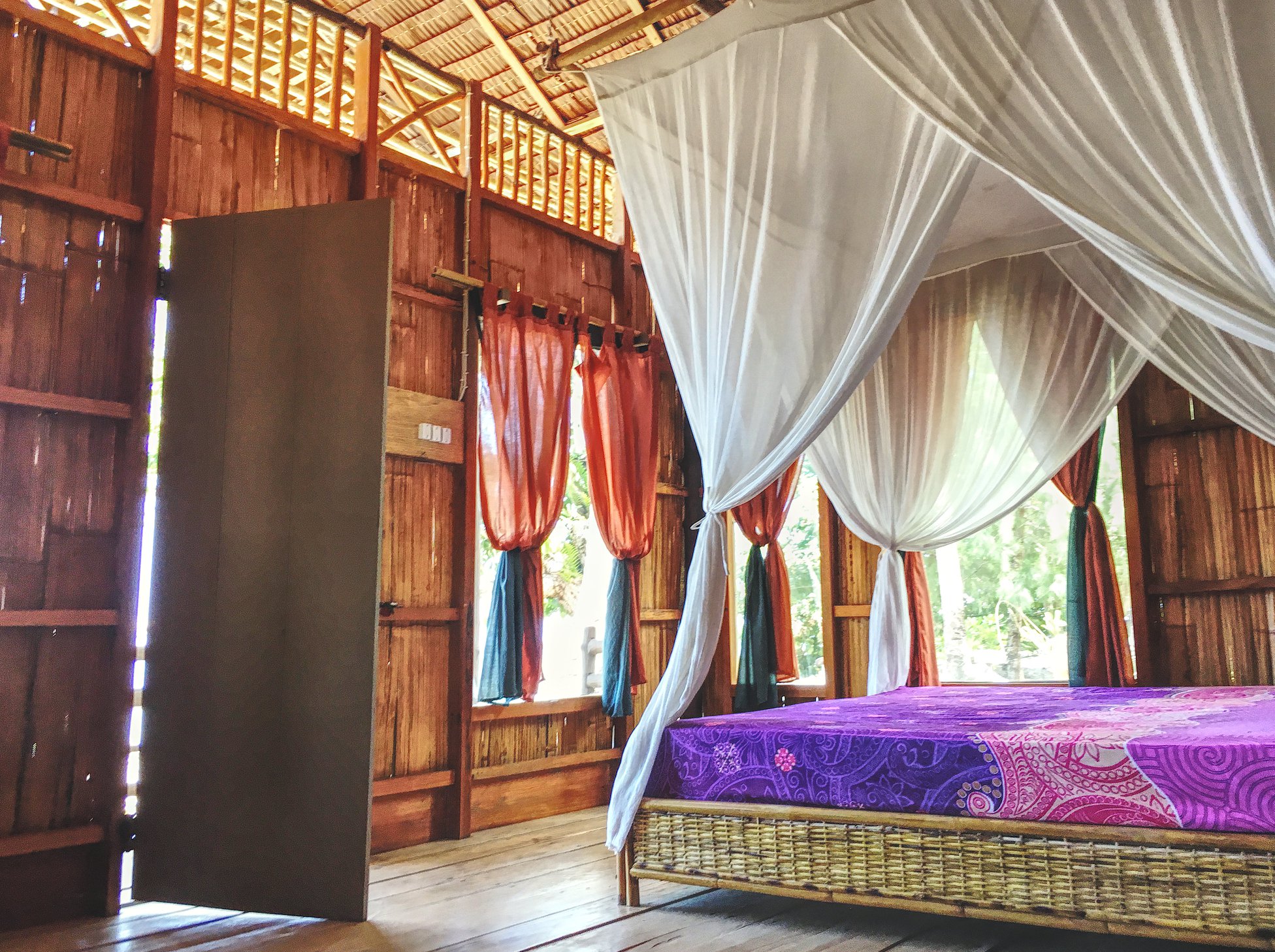 Zimmer mit Himmelbett aus Holz und Rattan, fließende Vorhänge bunt und wieß. Bild von Local Hideaways